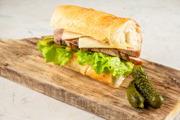 Cuban sandwich with pork, cucumbers and mustard on a wooden board.