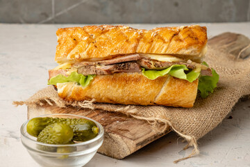 Cuban sandwich with pork and pickles on a serving board, light table.