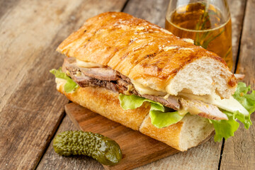 Homemade Cuban sandwich with pork, cheese and vegetables on an old wood table. Classic fast food.