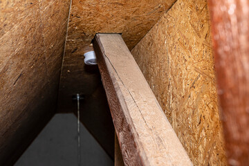 Roof truss visible in the attic house, painted brown with visible cracks in the wood, walls covered...