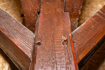 Roof truss visible in the attic house, painted brown with visible cracks in the wood, walls covered...