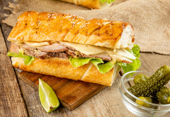Traditional Cuban sandwich with baked pork vegetables in a crispy bun with pickled cucumbers. The loaf is greased with butter.