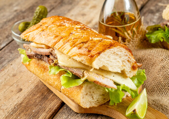 Traditional fast food cubano sandwich with baked pork in aromatic spices and cheese and pickled cucumbers in a toasted baguette with butter. Close-up.
