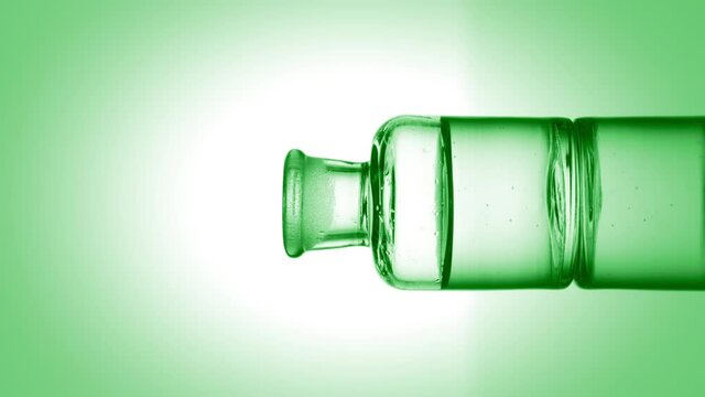 Green drop is falling into old fashioned bottle with green transparent liquid on green background | Abstract skincare cosmetics with hemp oil formulation concept