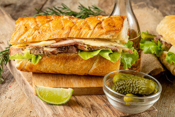 Traditional cubano sandwich with meat and cheese and vegetables on a wooden board.