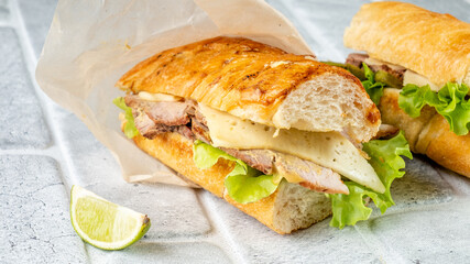 Sandwich with meat, cheese and vegetables in a baguette close-up.