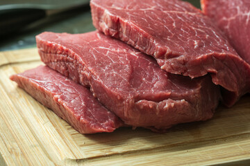 sliced raw roast beef meat on wooden cutting board closeup
