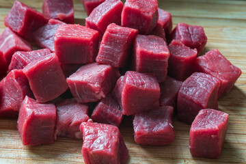 cubes of sliced raw roast beef meat on wooden cutting board closeup