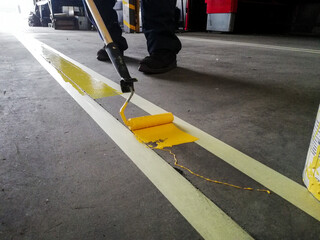 Closeup of a person painting a yellow line on a garage floor under the lights