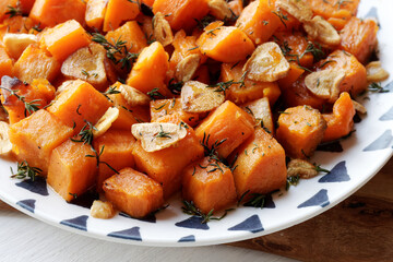 Roasted sweet potato plate. Baked root vegetable cubes with garlic and thyme herb.