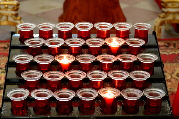 A close up on a set of candles with some of them being lit and giving warm light next to the altar seen in the middle of an old Catholic church in Poland during a Sunday mass 