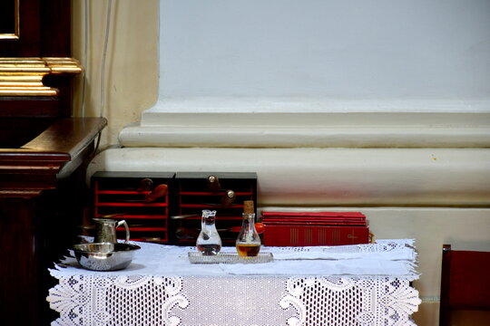 A close up on balsams, oils and books used during Catholic masses standing on a wooden table covered with a decorative cloth seen in an old Polish church after the conclusion of a Sunday mass