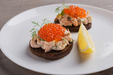 Close up Toast skagen - classic Swedish appetizer. Sandwich with shrimps and caviar served on white plate. Nordic cuisine. Selective focus.