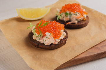 Toast skagen - classic Swedish appetizer. Healthy snack from bread with shrimps and caviar on light wooden background. Selective focus.