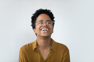 Overjoyed millennial African American woman in eyeglasses laughing, showing positive emotions near white wall. Happy female client demonstrating perfect whitening smile, isolated on studio wall.
