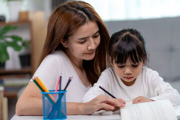 Obraz premium Beautiful Asian woman helping her daughter with homework at home.