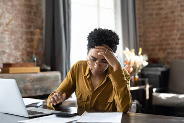 Unhappy frustrated young African American woman feeling stressed managing financial affairs or mistakes, suffering from lack of money calculating business expenditures, accounting, bankruptcy concept.