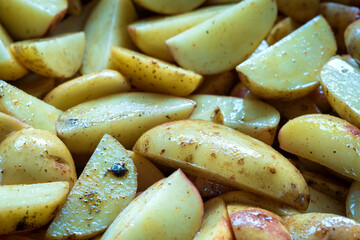 fresh raw potatoes wedges mixed with oil and spices ready for baking closeup