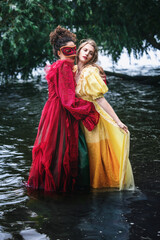 two women in historic gowns standing the water and hugging