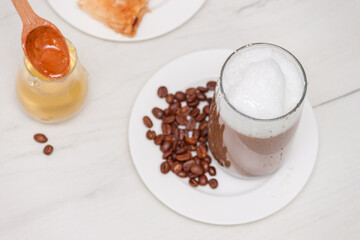 Glass coffee with foam milk with honey on white wooden table.