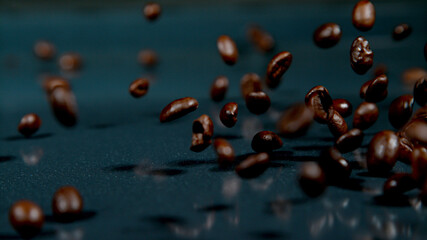 MACRO: Dark roasted arabica coffee beans fall onto the shiny black surface.