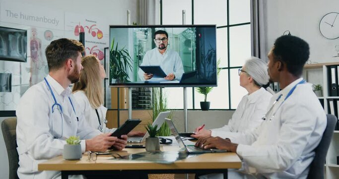 Attractive experienced hardworking multiethnic team of doctors holding online meeting with main medical manager on digital screen in modern clinic office