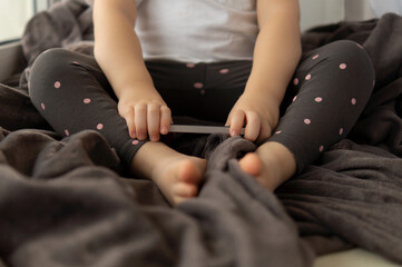 Cropped image of a little girl sitting on a window in a soft blanket and using a cell phone.