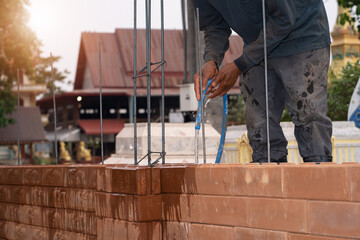 Construction worker holding a hose to water bricks, man building a brick wall, builder carrying out a construction project by himself.