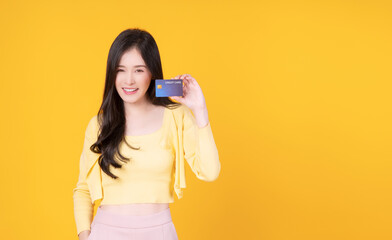 Cheerful asian woman showing credit card transaction standing copy space over isolated yellow...