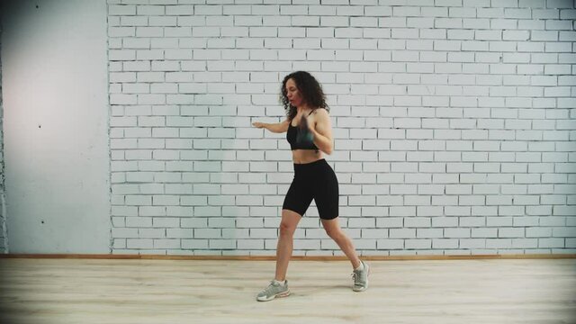 Workout in sports studio - young woman with curly hair training her hands by pulling the weight
