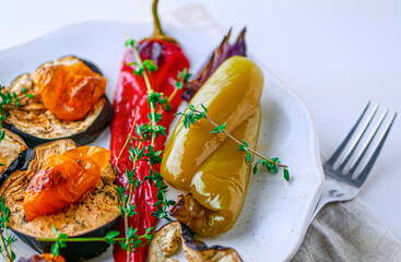 Roasted vegetables with herbs in a white plate with a fork on a background, close-up, copy space. Diet Vegetable Dinner with Baked Peppers and Eggplant
