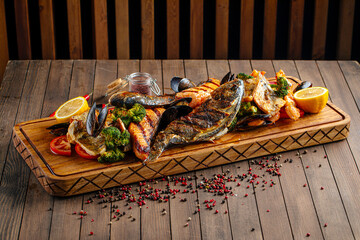 Side view on assorted grilled fish set on wooden serving board