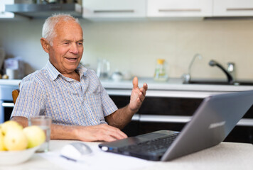 Elderly man sitting at table talking through internet