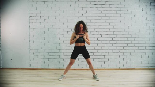 Workout in sports studio - young woman with curly hair training her hands by working with a dumbbell
