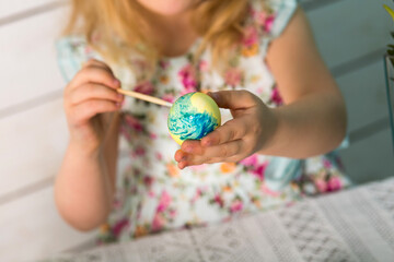 Cute little girl blonde paints colored Easter eggs with a tassel. Easter theme