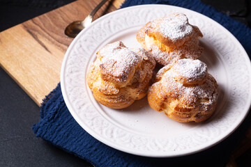 Food concept Homemade fresh baked Choux a la creme, Cream Puff, Choux Cream in white ceramic plate on black background with copy space