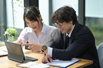 Photo of young businesspeople working together at the wooden working desk with a digital tablet and clipboard.