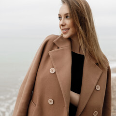 portrait of a young happy woman in coat and glasses outdoor on the beach autumn spring