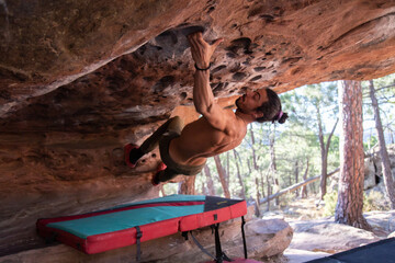 From below back view of young sportsman with naked torso climbing natural rocky roof 