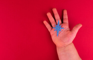 Christmas blue star in children's hand on a red background. Copy space.