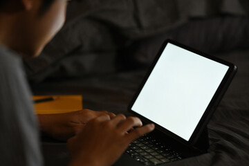 Photo of a freelance man using a white blank screen digital tablet in the bedroom.