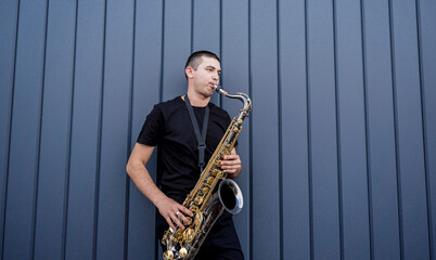 Fototapeta premium Young street musician playing saxophone near the big blue wall