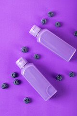 Shower gel with blueberry in two bottles on purple. Mockup with unlabeled body care product or wash liquid detergent with natural ingredient. Monochrome flat lay