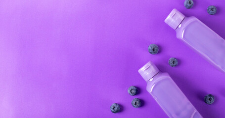 Web banner with shower gel with blueberry in two bottles on purple. Mockup with unlabeled body care product or wash liquid detergent with natural ingredient. Monochrome background
