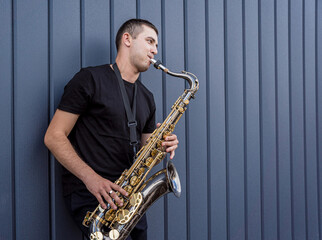Naklejka premium Young street musician playing saxophone near the big blue wall