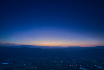 Blue orange gradient sky over mountain range and village in an evening 
