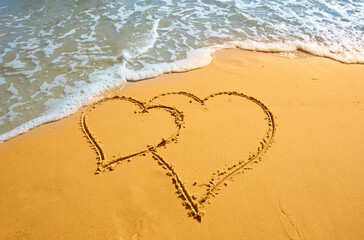 Two hearts handwritten on sand of tropical beach