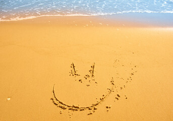 Funny smile face drawn on wet sand