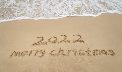 Fototapeta na wymiar 2022 Merry Christmas handwritten in sand on beach