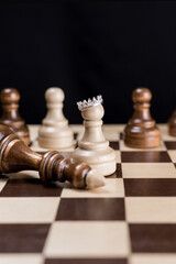 A white chess pawn with a crown on the chessboard, next to it lies the defeated black chess king.Vertical banner.The concept of success and self-belief. Motivation.